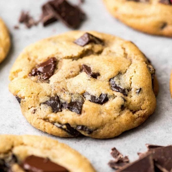 side view of the best chocolate chip cookie recipe ever one cookie with melty chocolate chips surrounded by three other cookies and chopped chocolate