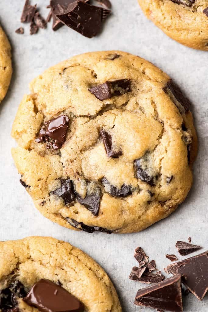 Overhead view of the best chocolate chip cookie recipe ever one cookie with melty chocolate chips surrounded by three other cookies and chopped chocolate