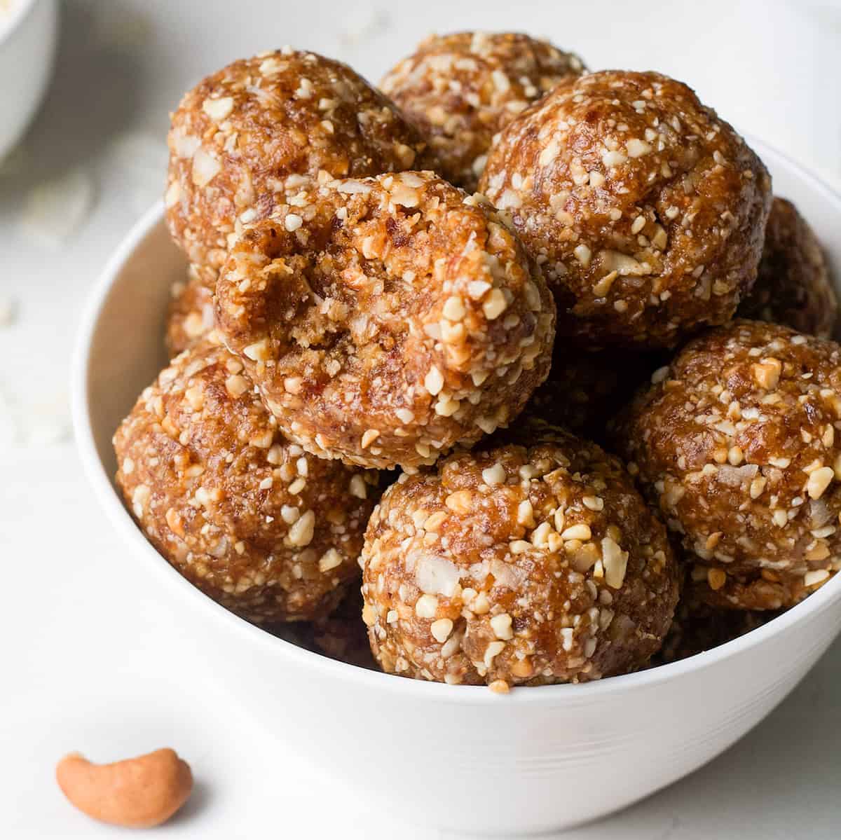a bowl of coconut date balls, the top one has a bite taken out of it
