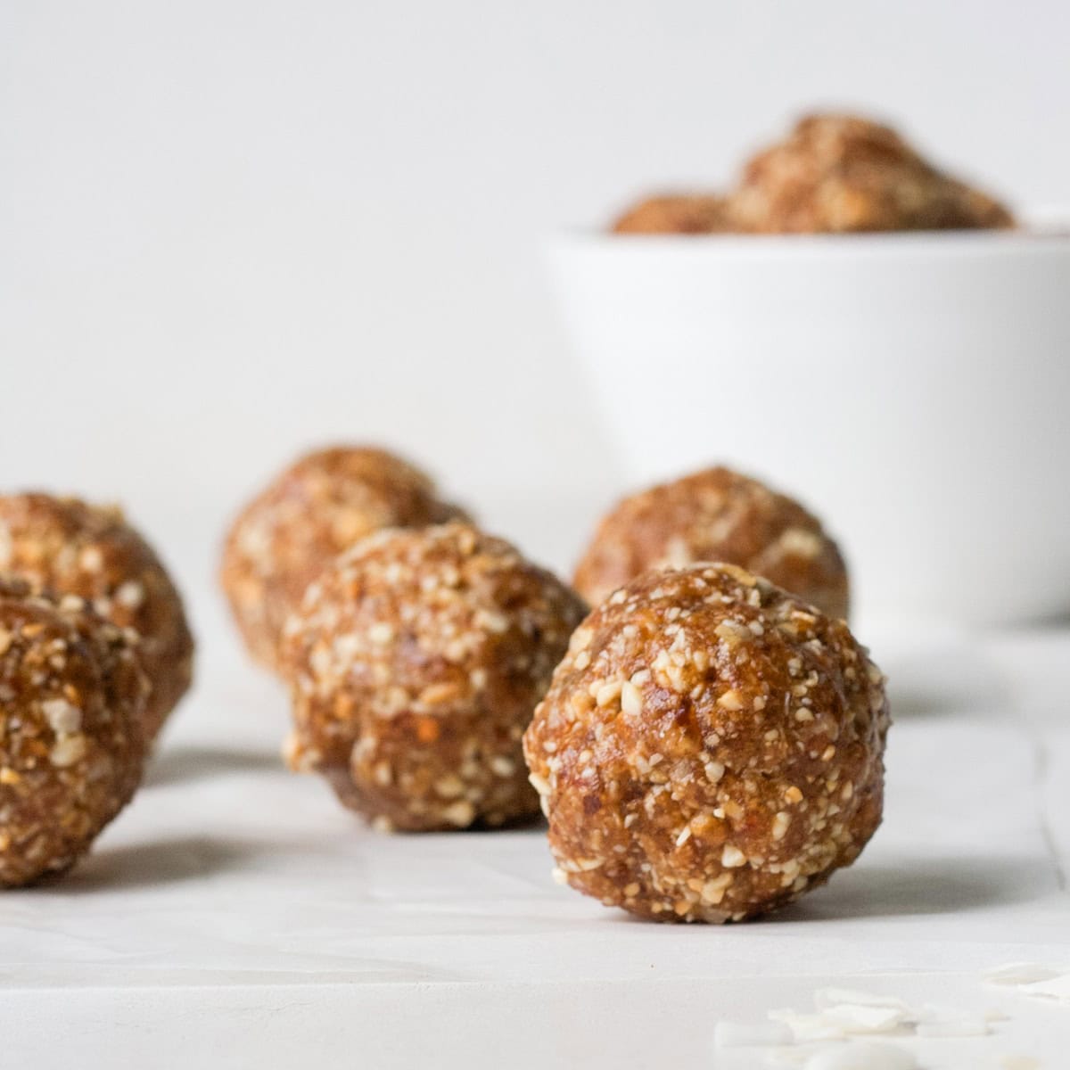 four Cashew Coconut Date Balls in front of a bowl of date balls.