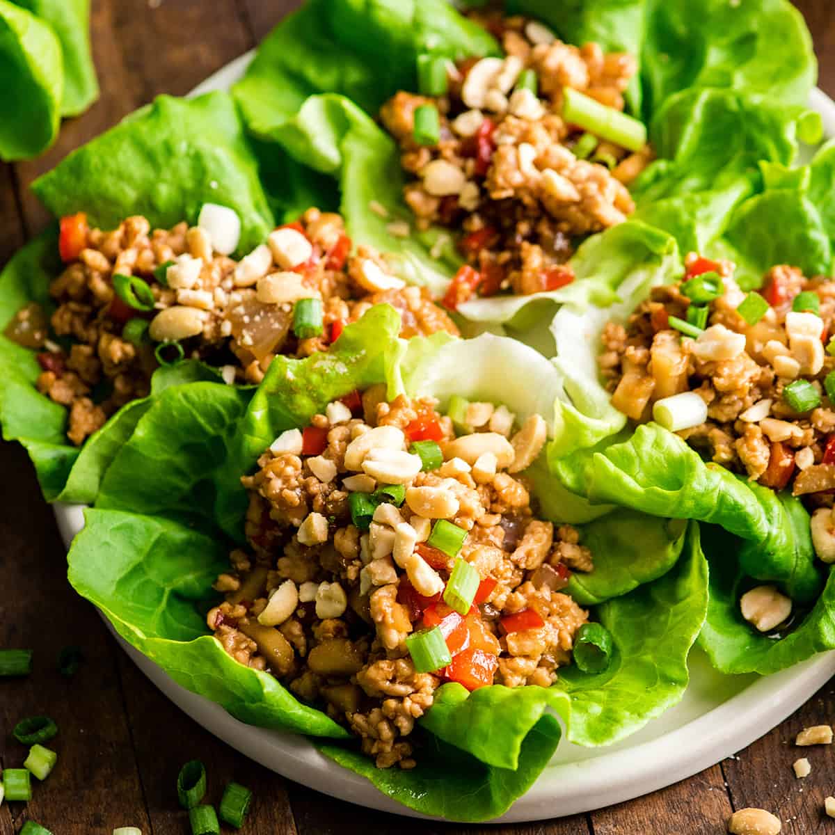 front view of four Asian Chicken Lettuce wraps on a plate with peanuts sprinkled on top