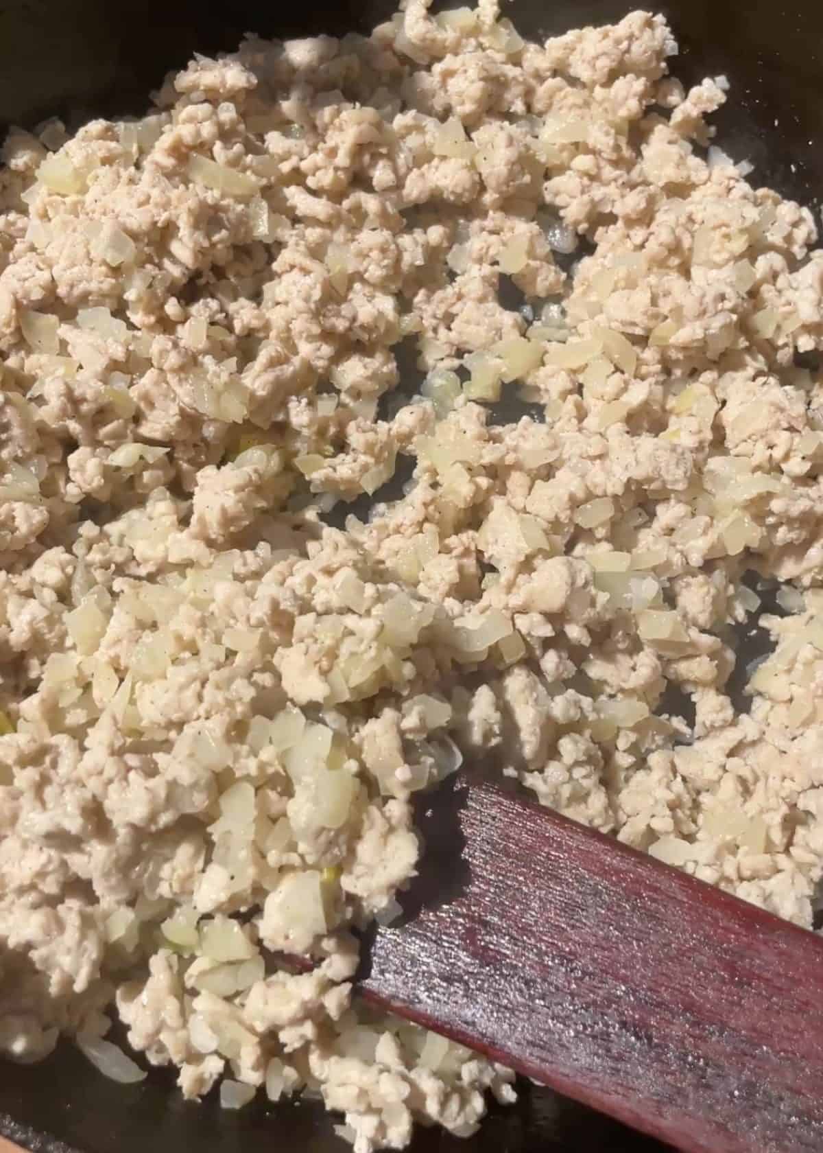 making lettuce wraps recipe - ground chicken, onion and minced garlic in a cast iron skillet after cooking being stirred with a wooden spatula
