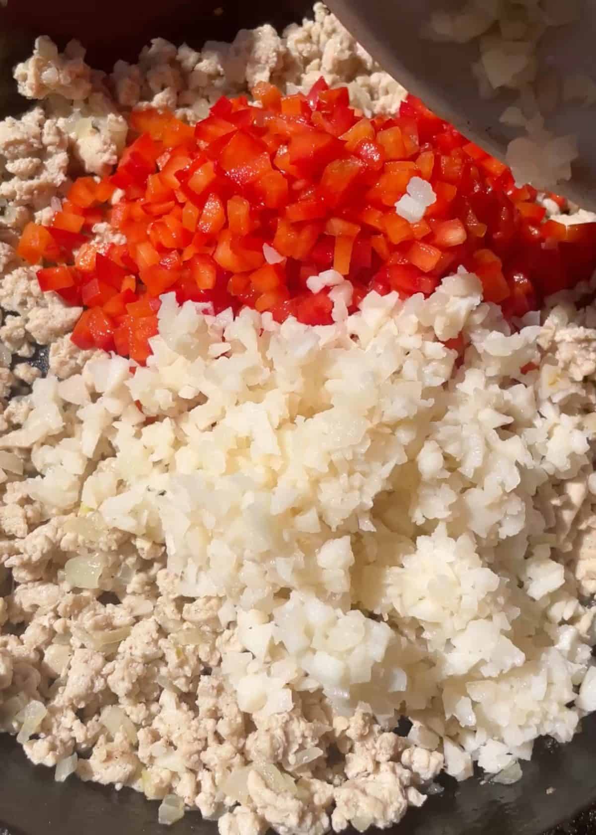 making lettuce wraps recipe -finely chopped red bell pepper and water chestnuts added to the cooked ground chicken mixture in a cast iron skilling before cooking the vegetables