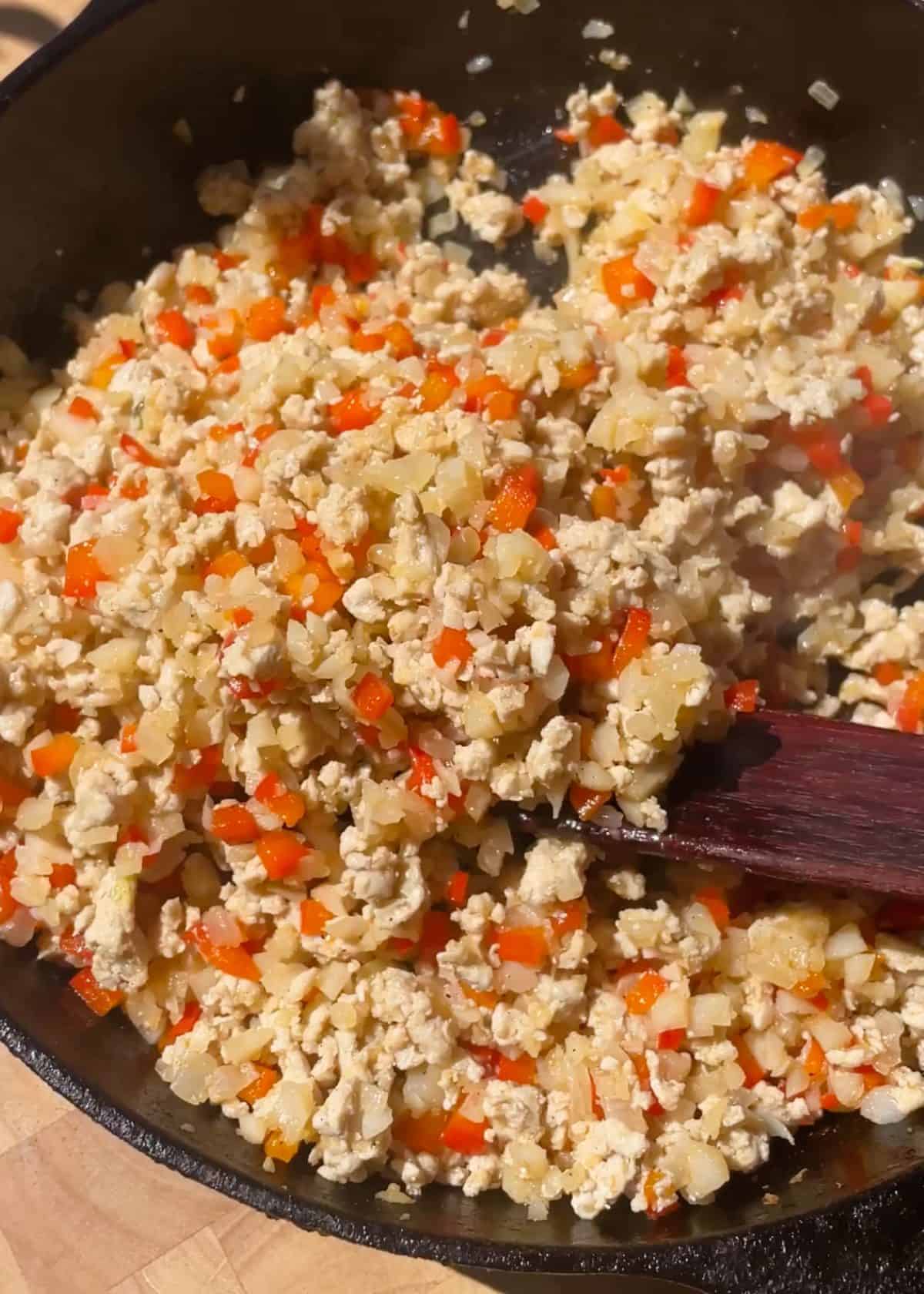making lettuce wraps recipe - filling after the vegetables have been stirred in and cooked in a cast iron skillet being stirred with a wooden spatula