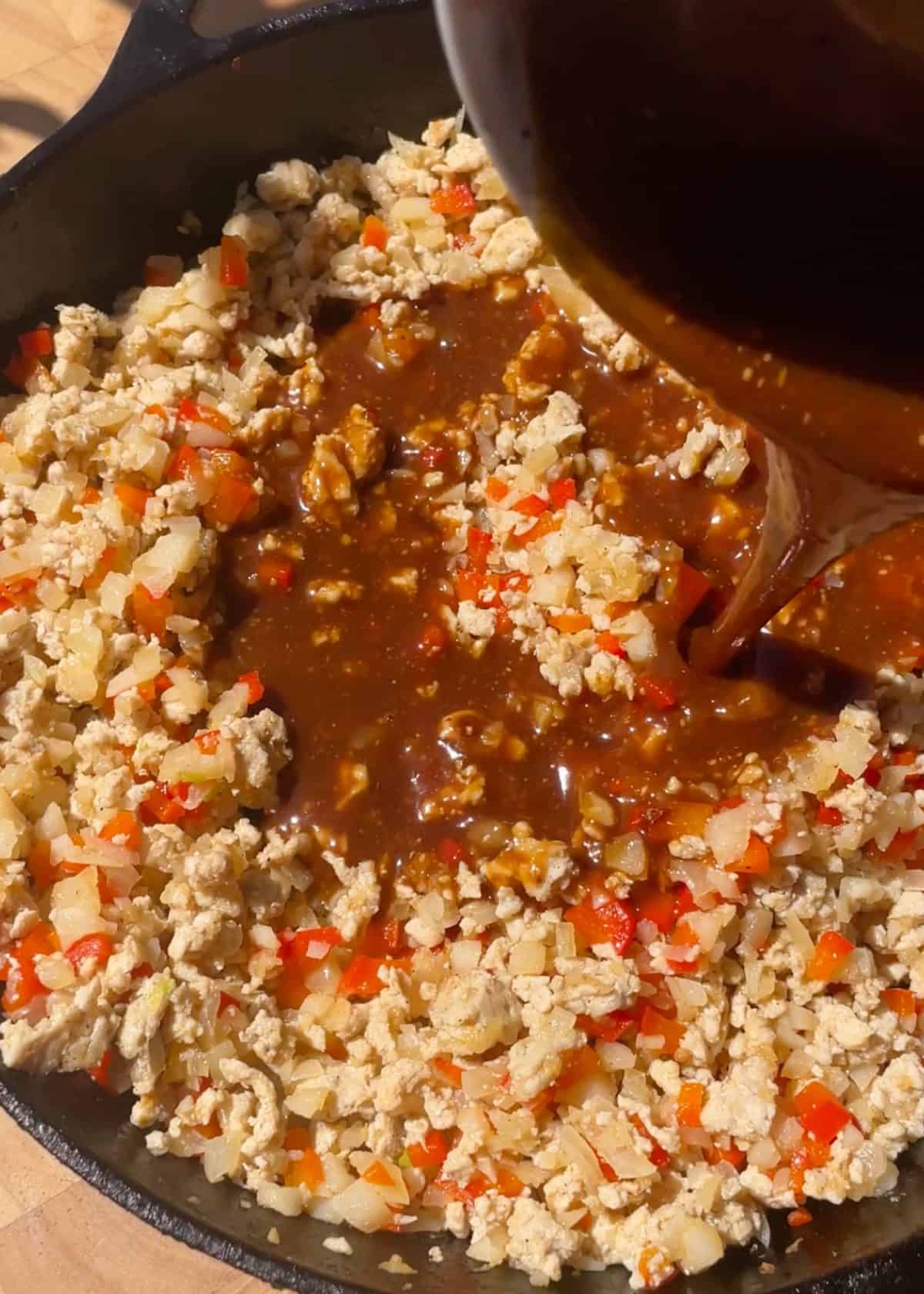 making asian chicken lettuce wraps recipe - sauce being poured into the filling mixture in a cast iron skillet