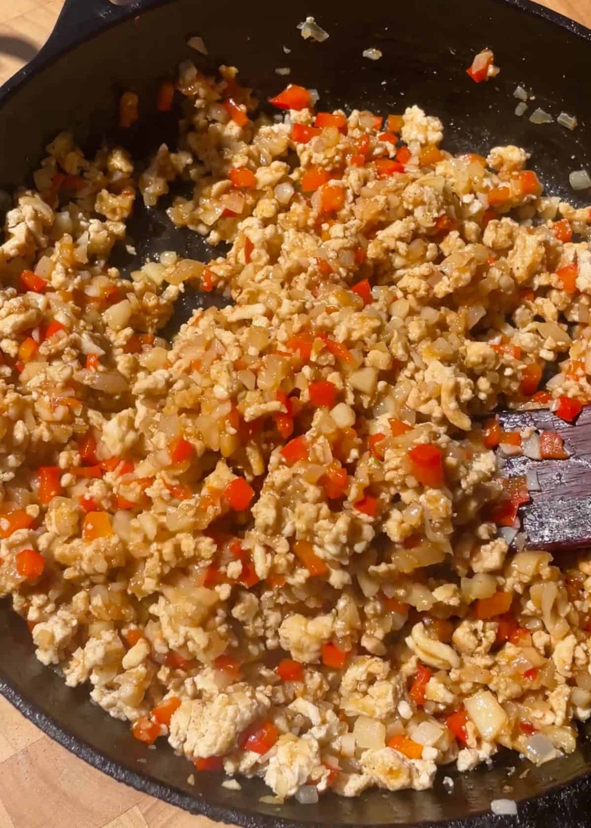 making asian chicken lettuce wraps recipe - final filling mixture after cooking in the sauce being stirred by a wooden spatula in a cast iron skillet