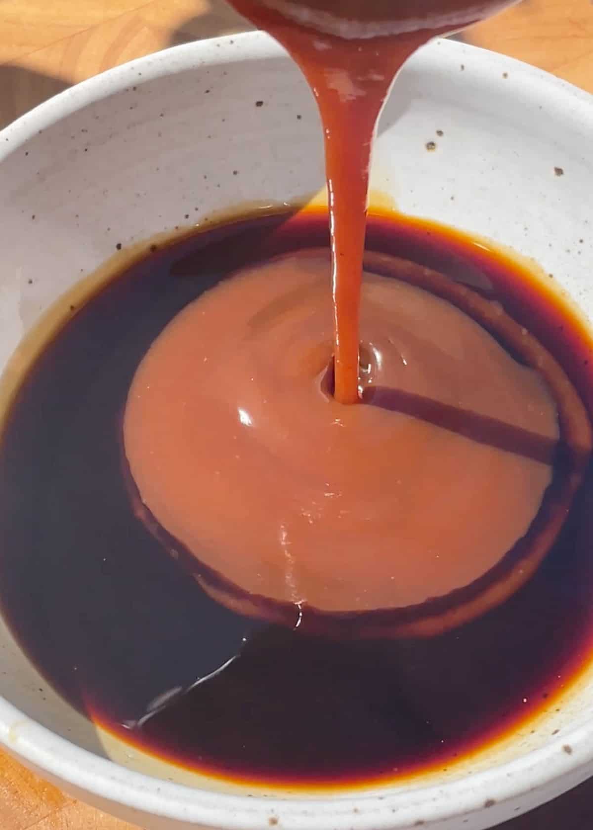 making lettuce wraps sauce - hoisin sauce being poured into a ceramic bowl with soy sauce already in it