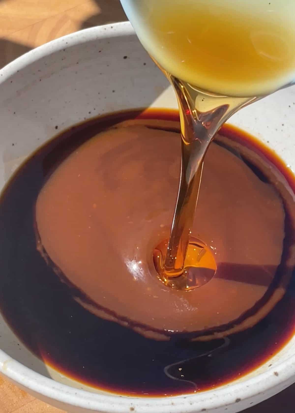 making lettuce wraps sauce - rice vinegar being poured into a ceramic bowl with soy sauce and hoisin sauce already in it