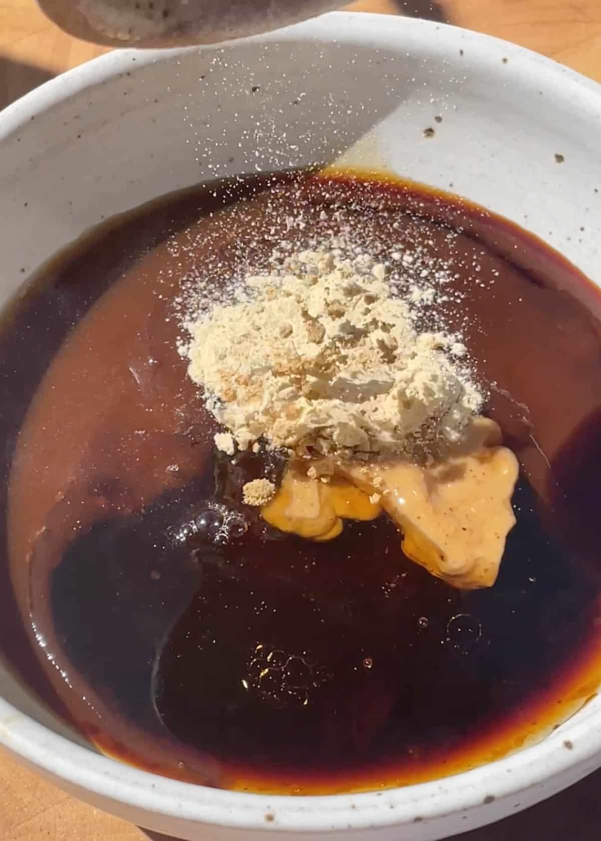 making lettuce wraps sauce - peanut butter, powdered garlic, powdered ginger added to the sauce mixture in a ceramic bowl before mixing