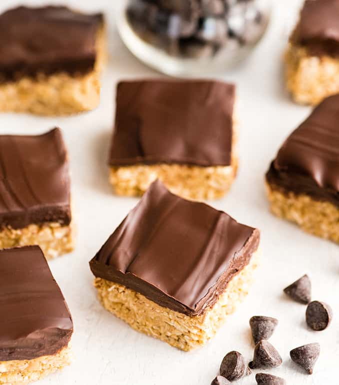 overhead view of seven No-Bake Oatmeal Bars with Peanut Butter & Coconut laid out on a white surface with chocolate chips around them. 