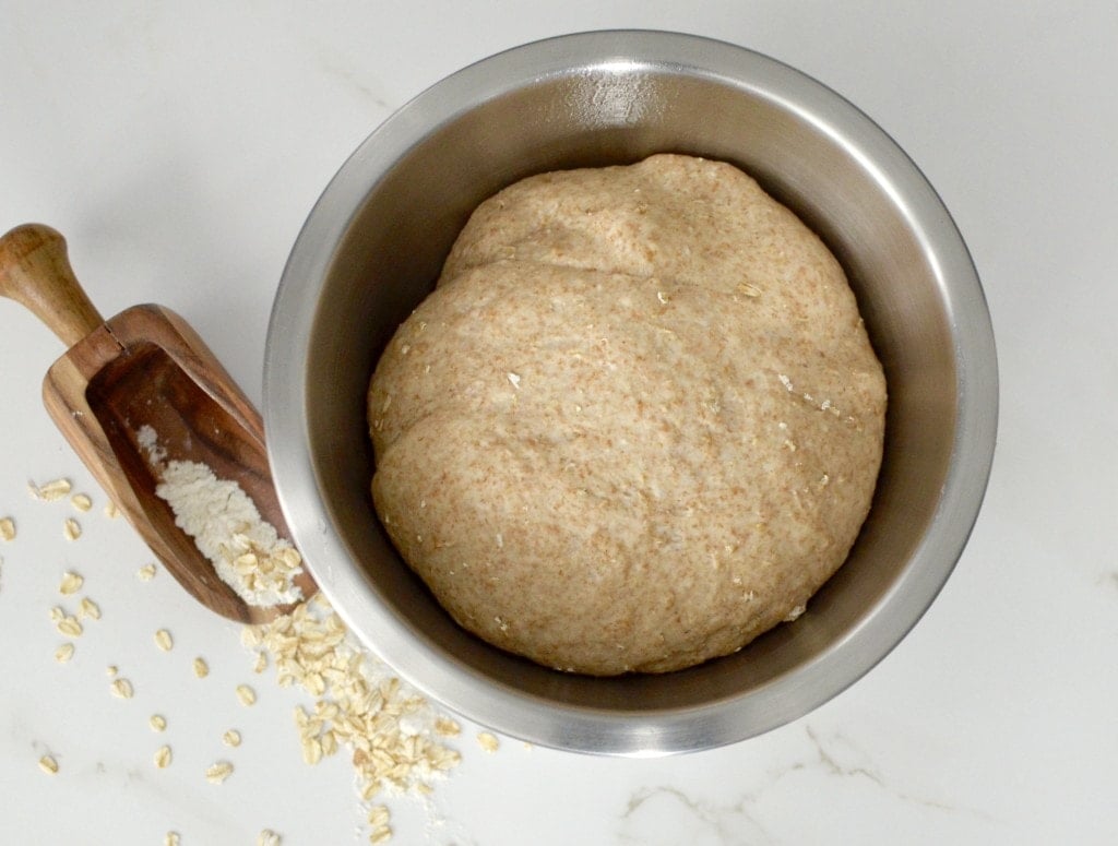 Overview of bowl with bread dough with oats in background. 