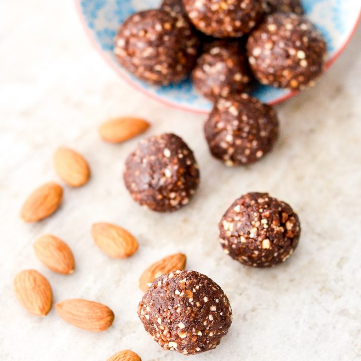 overhead view of 10 almond butter protein balls spilling out of a bowl with almonds around them