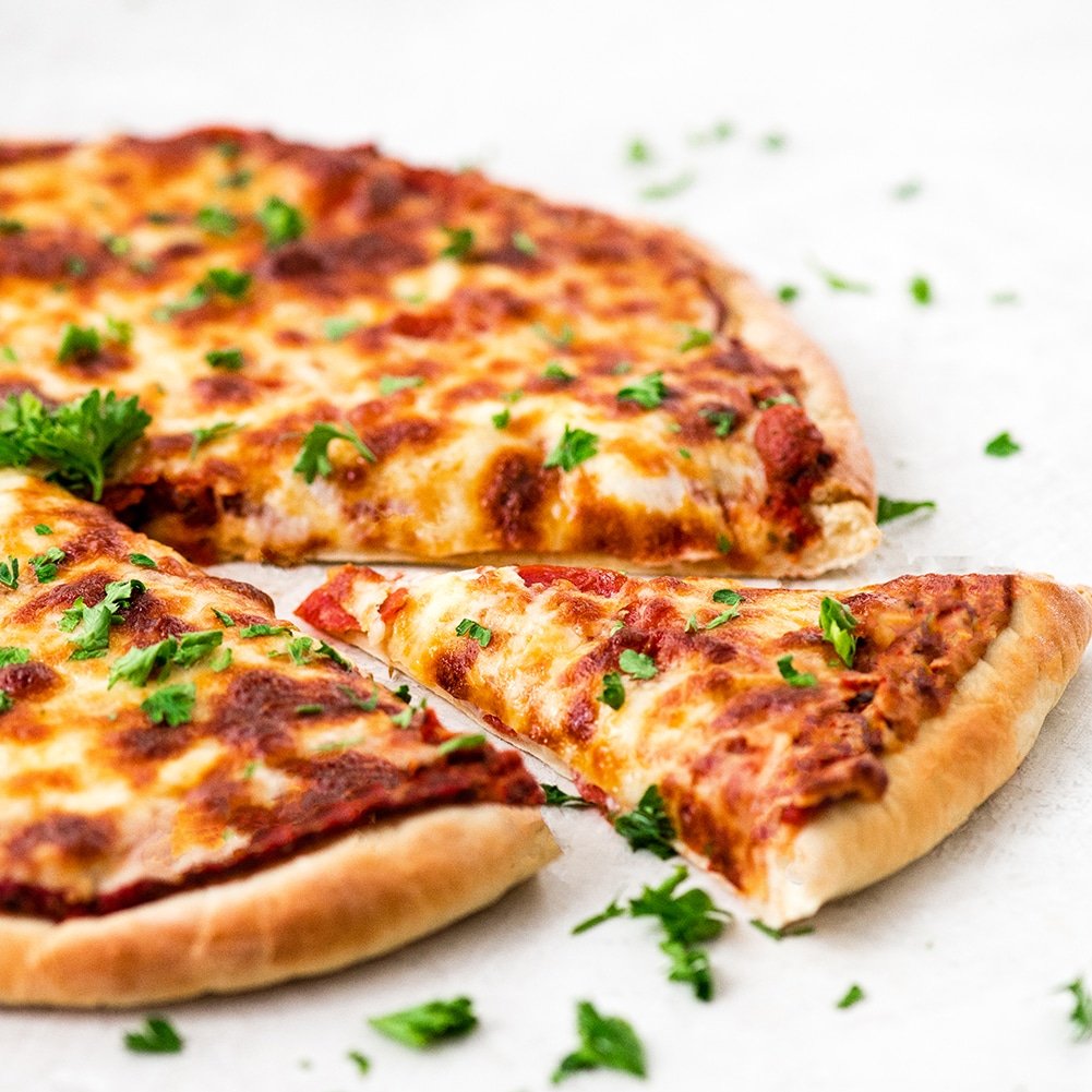 front view of a finished homemade pizza with one piece cut out and removed from the pizza showing the baked Easy Homemade Pizza Dough