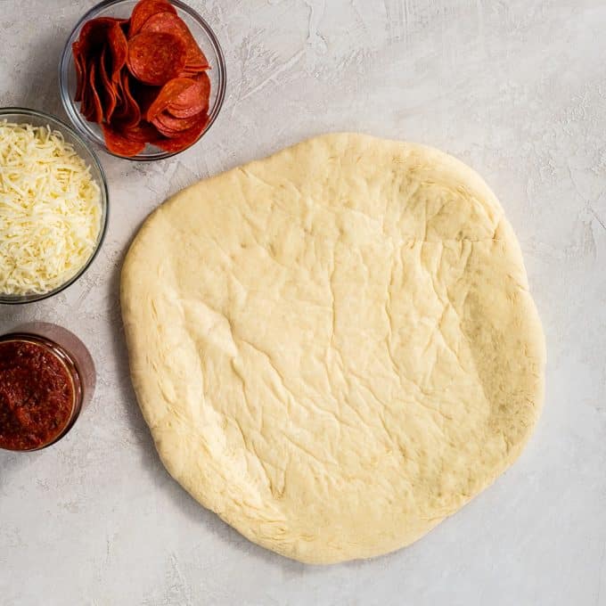 Overhead view of rolled and pre-baked Easy Homemade Pizza Dough surrounded by pizza sauce, cheese and toppings 