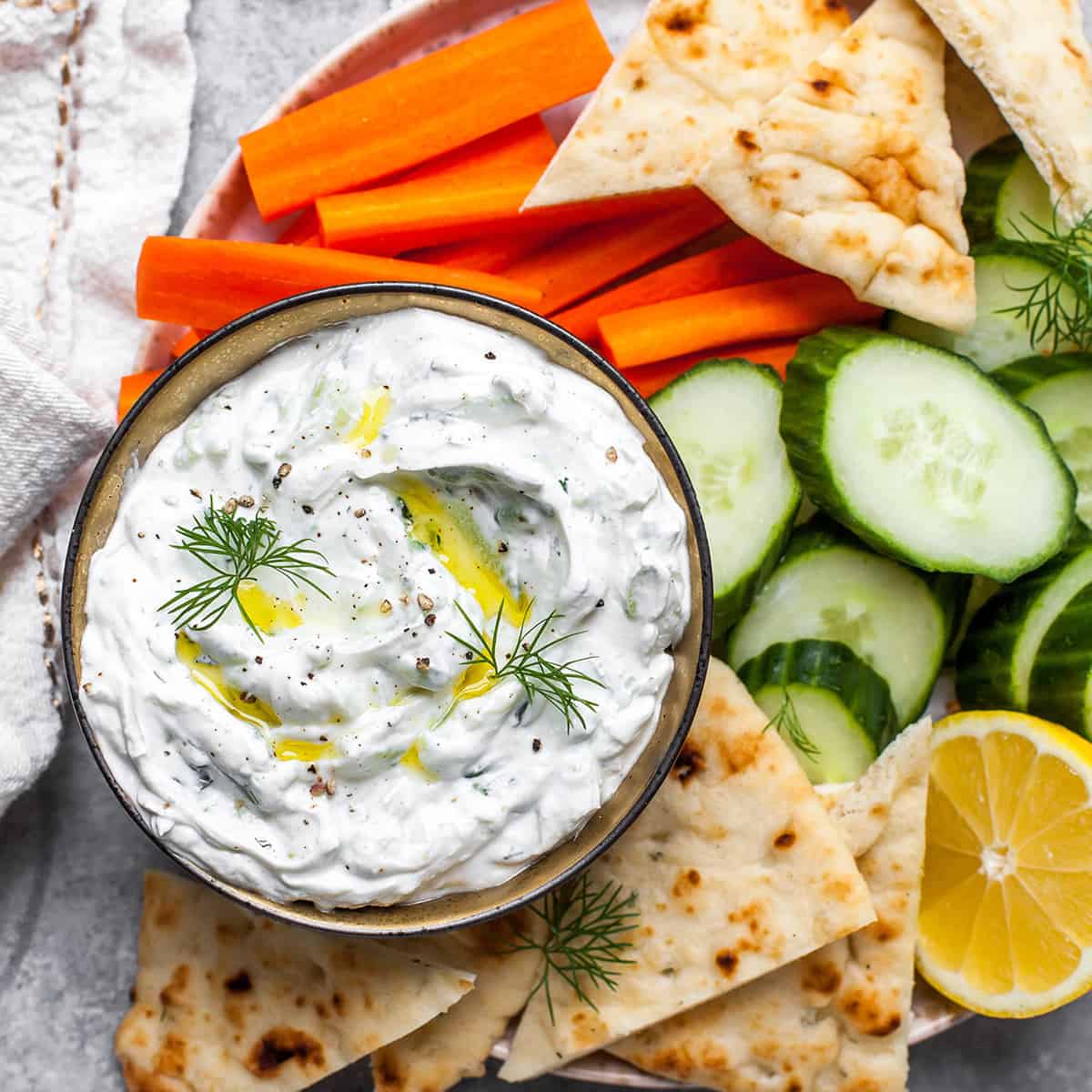 overehead photo of a bowl of homemade tzatziki sauce with pita and vegetables around it