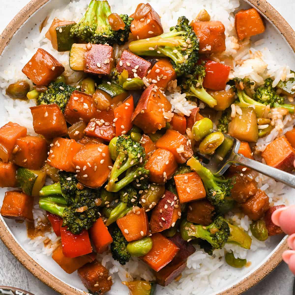 a fork taking a bite of Sweet Potato Stir Fry on a plate over rice 