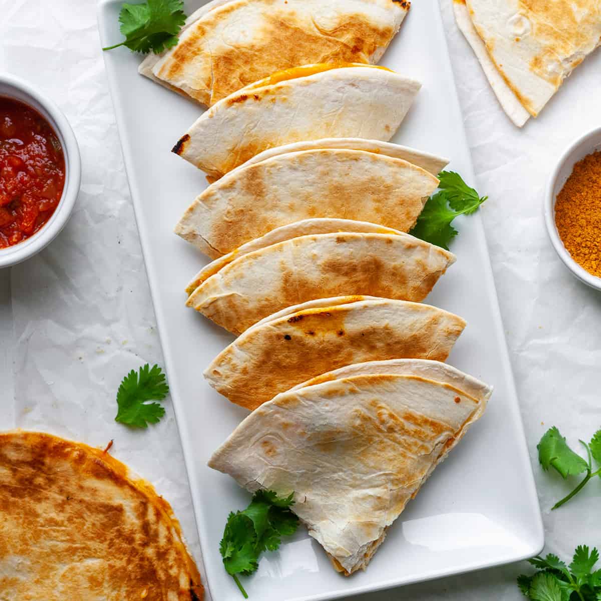 overhead view of 7 triangular pieces of chicken quesadilla in a line on a serving plate.