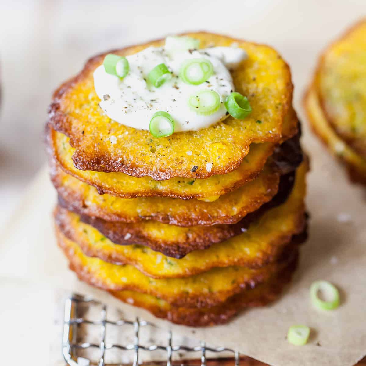 front view of a stack of 7 corn and zucchini fritters topped with sour cream
