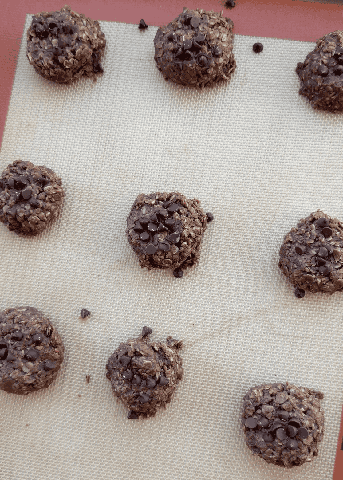 9 healthy no bake cookies topped with mini chocolate chips on a baking sheet lined with a silicone baking mat