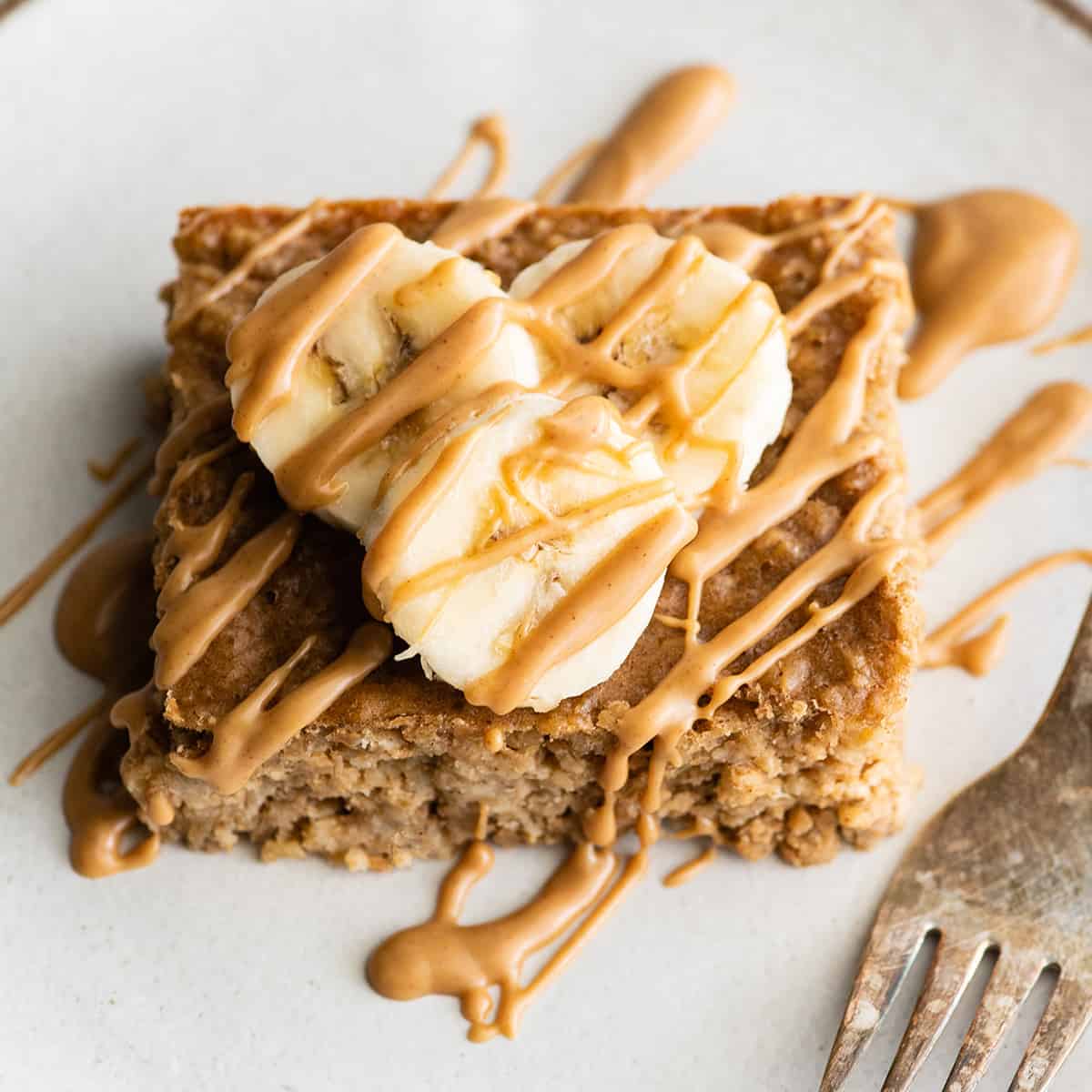 front view of a piece of peanut butter banana baked oatmeal on a plate with bananas on top and drizzled with peanut butter
