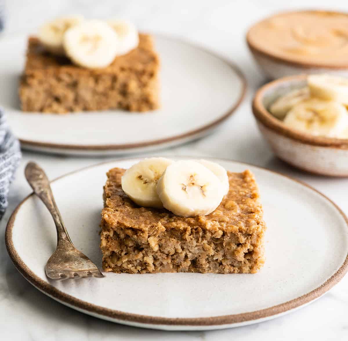 front view of a piece of peanut butter banana baked oatmeal on a plate with bananas on top