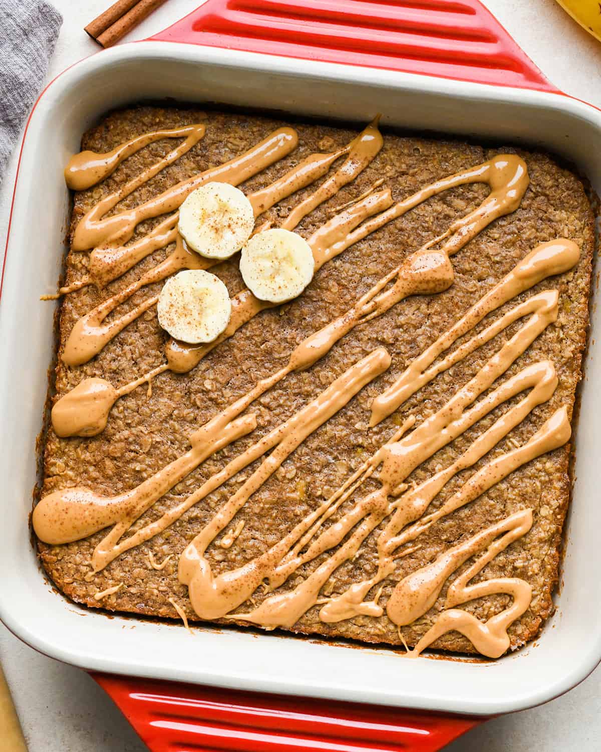Peanut Butter Banana Baked Oatmeal in a baking dish drizzled with peanut butter, topped with sliced bananas and cinnamon