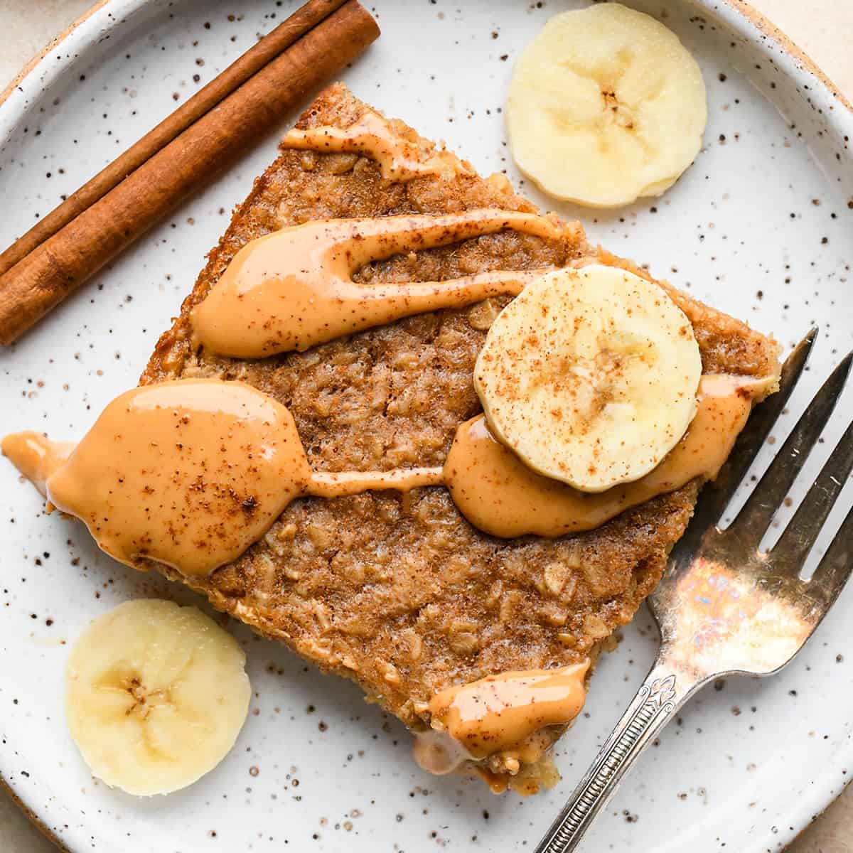 a piece of Peanut Butter Banana Baked Oatmeal on a plate with a drizzle of peanut butter, bananas and a fork