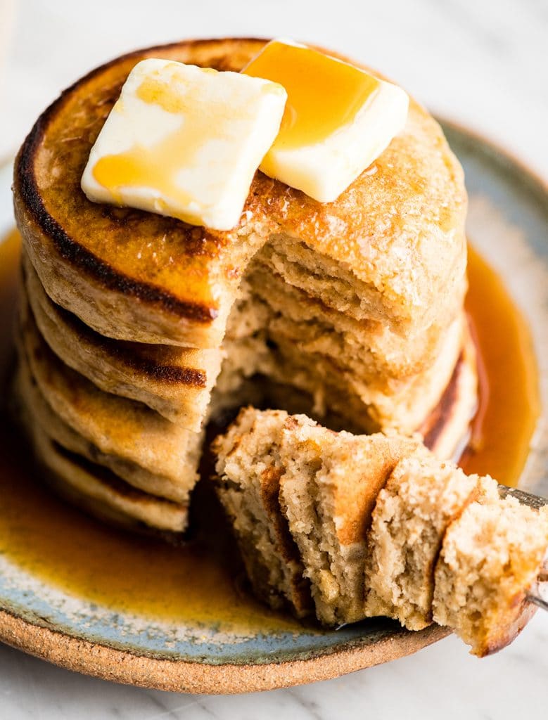 Up close overhead/front view of a stack of four Greek yogurt pancakes that have been cut into and the bite is resting on the plate on a fork