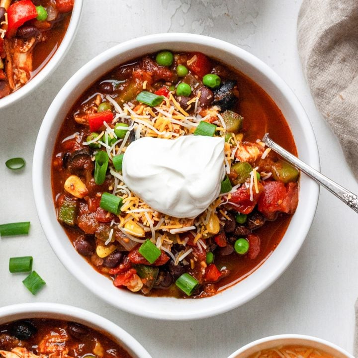 overhead view of a bowl of chicken chili with sour cream, cheese and green onions