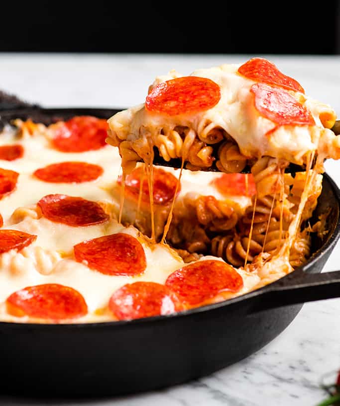 vista frontale di un pezzo di casseruola di pizza che viene tirato fuori dalla padella mentre si staccano anche i fili di formaggio