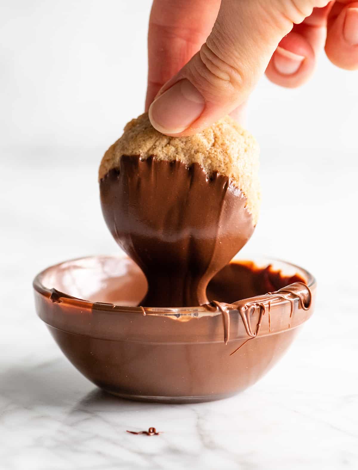 a hand dipping a flourless peanut butter cookie in a bowl of melted chocolate