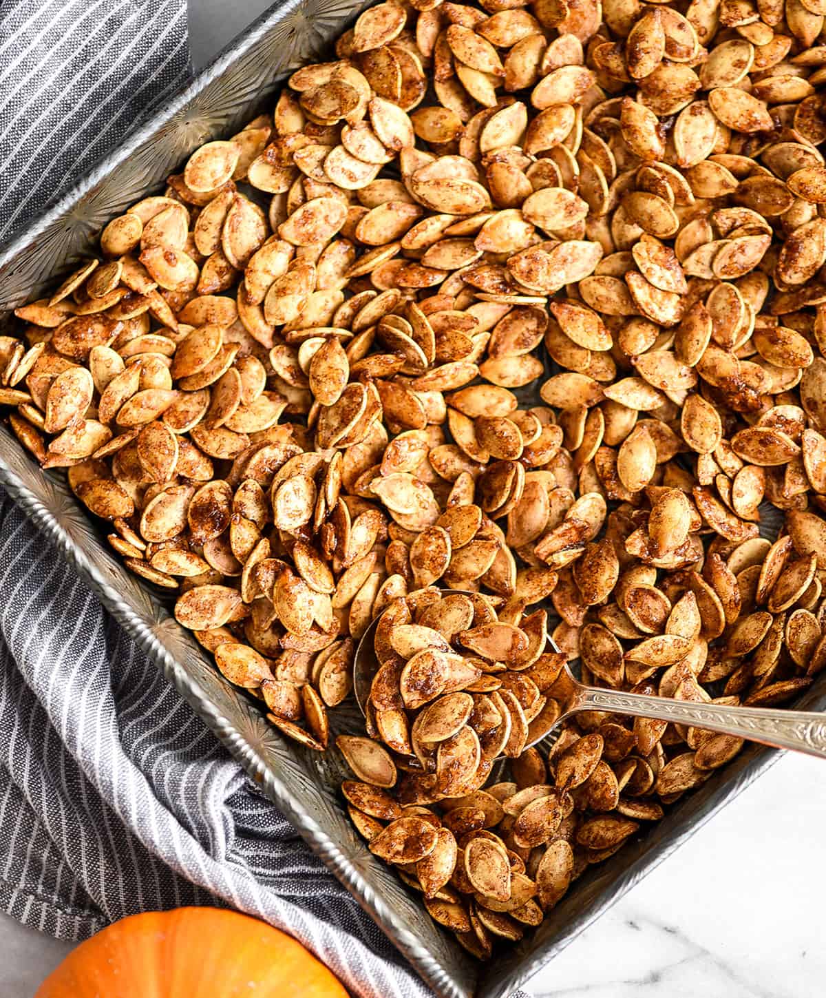 Overhead view of a spoon scooping Homemade Cinnamon Sugar Pumpkin Seeds out of a baking pan