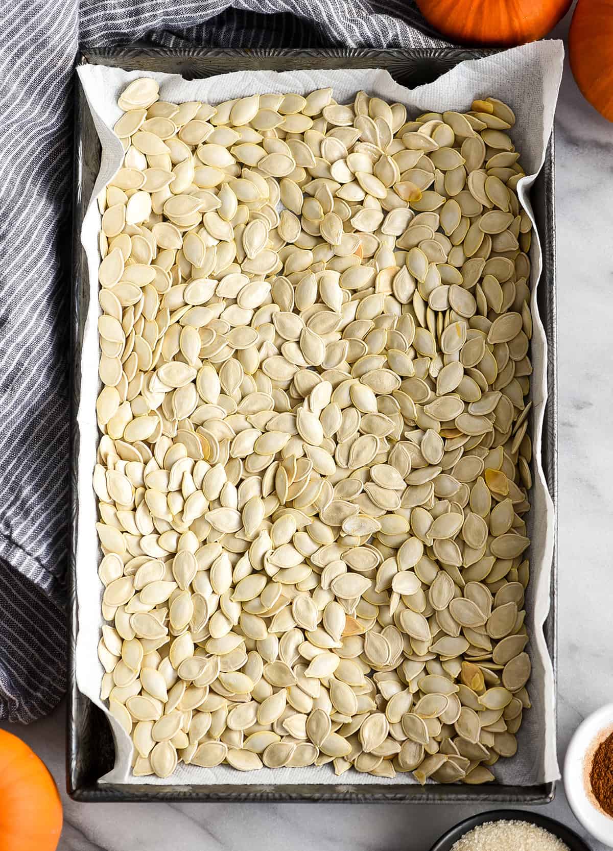 overhead view of pumpkin seeds drying in a baking pan on a paper towel