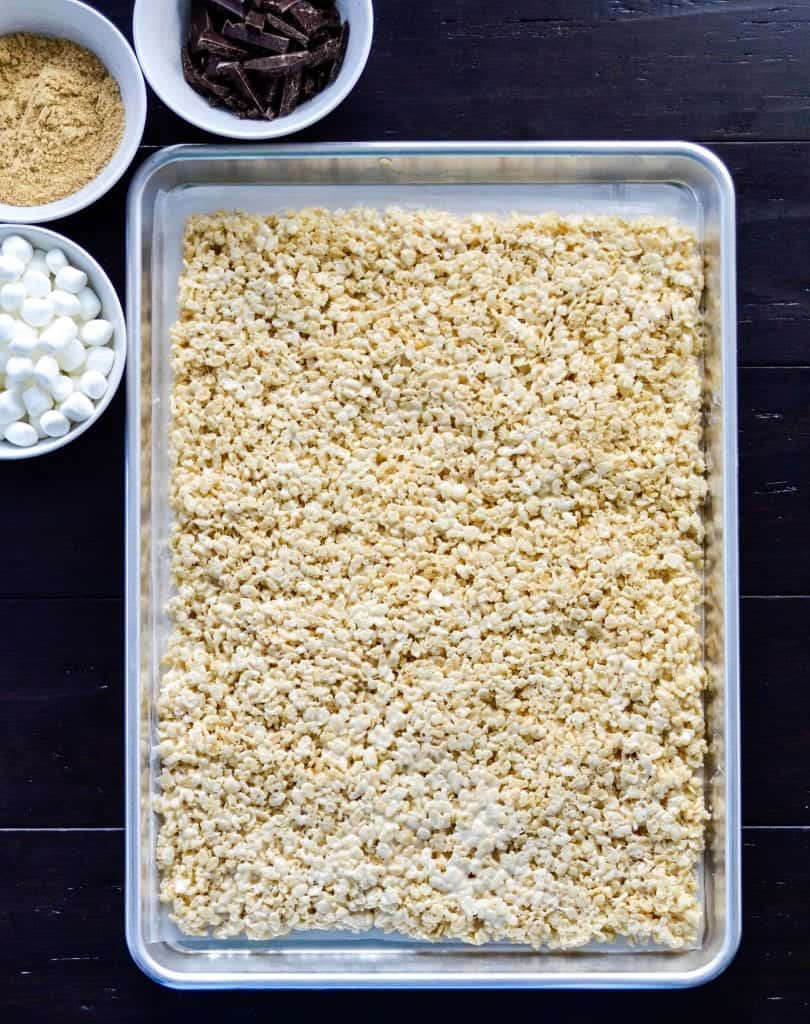 Overhead view of a large baking pan spread out with rice krispie treats with other ingredients around it in the making of Dessert Sushi 