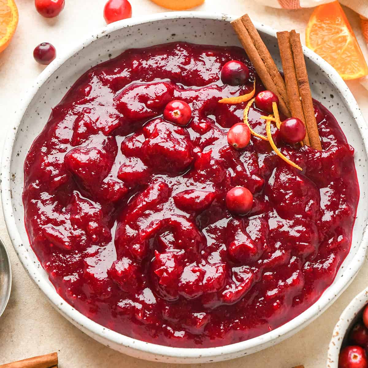 a bowl of homemade cranberry sauce garnished with fresh cranberries, orange peel and cinnamon sticks