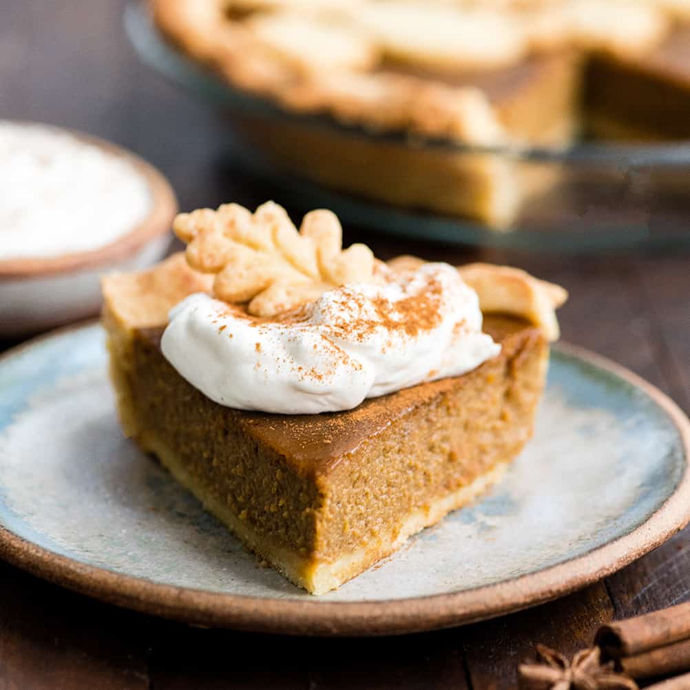 Front view of a slice of Dairy-Free Pumpkin Pie on a plate topped with whipped cream