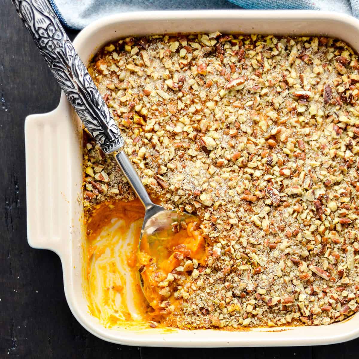 Overhead view of a healthy sweet potato casserole in a square baking dish with some missing and a spoon scooping more out of it 