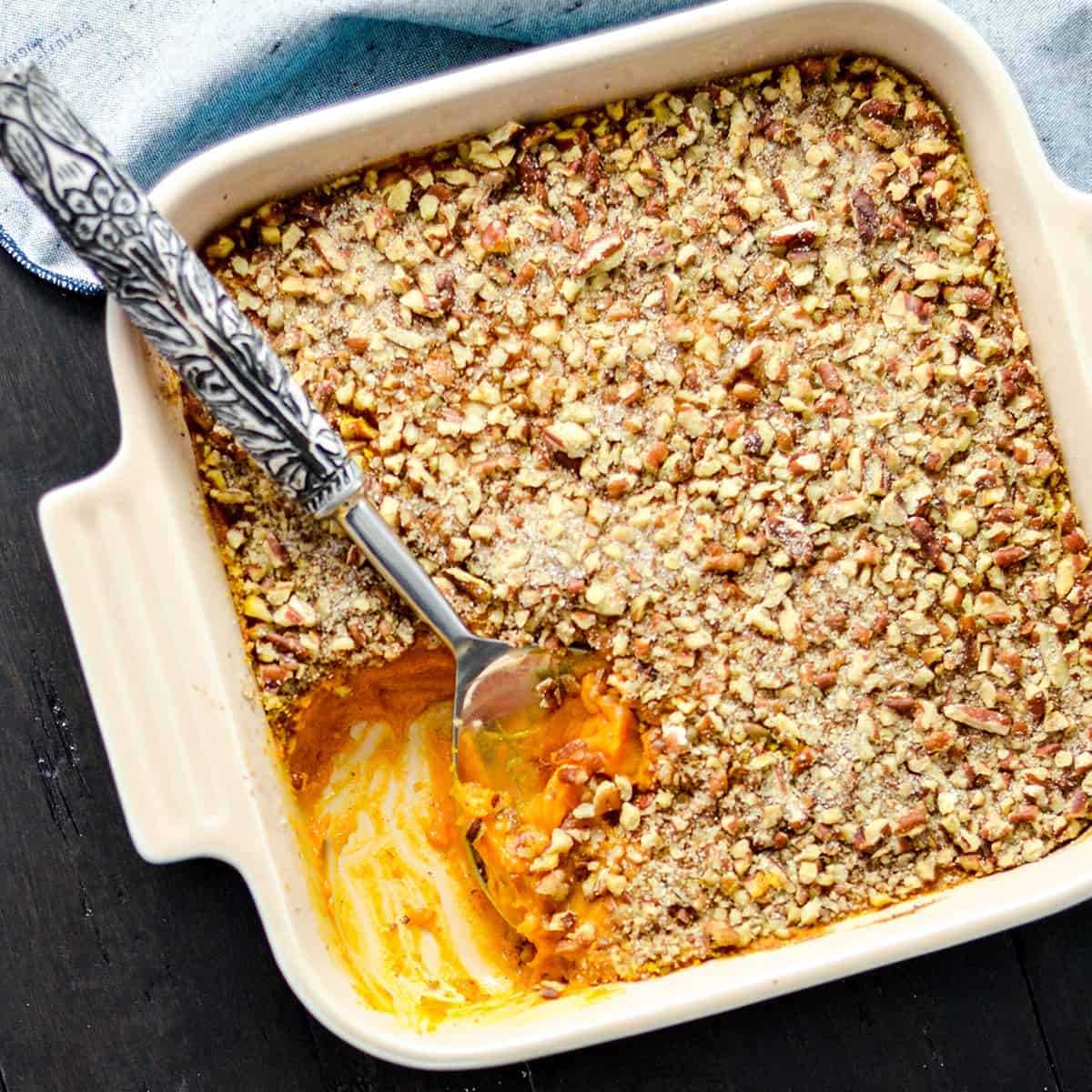 Overhead view of a healthy sweet potato casserole in a square baking dish with some missing and a spoon scooping more out of it 
