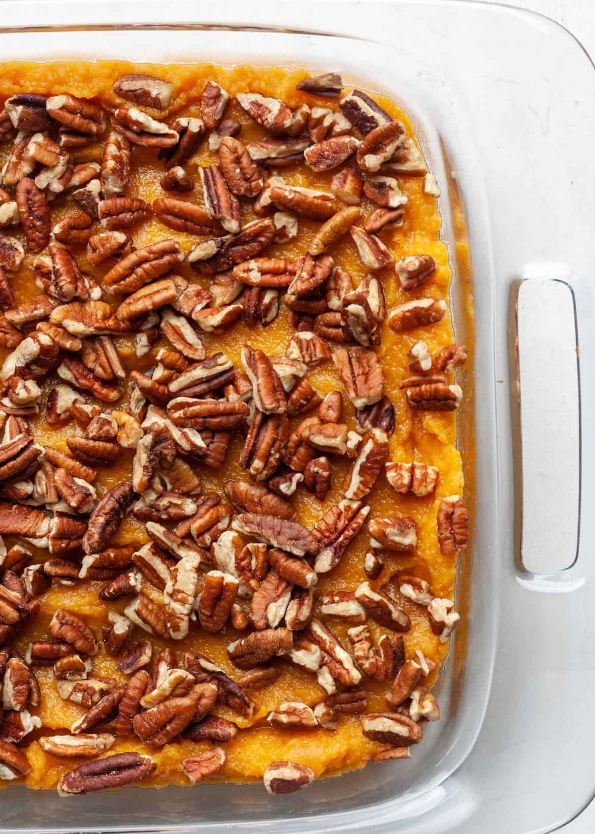 healthy sweet potato casserole recipe in a glass baking dish topped with pecans.