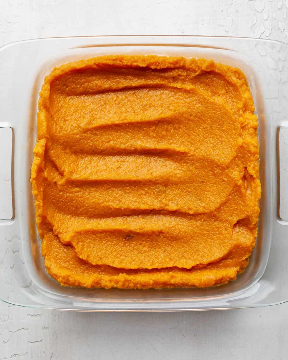 making healthy sweet potato casserole recipe - sweet potato casserole filling spread into a square glass baking dish before baking