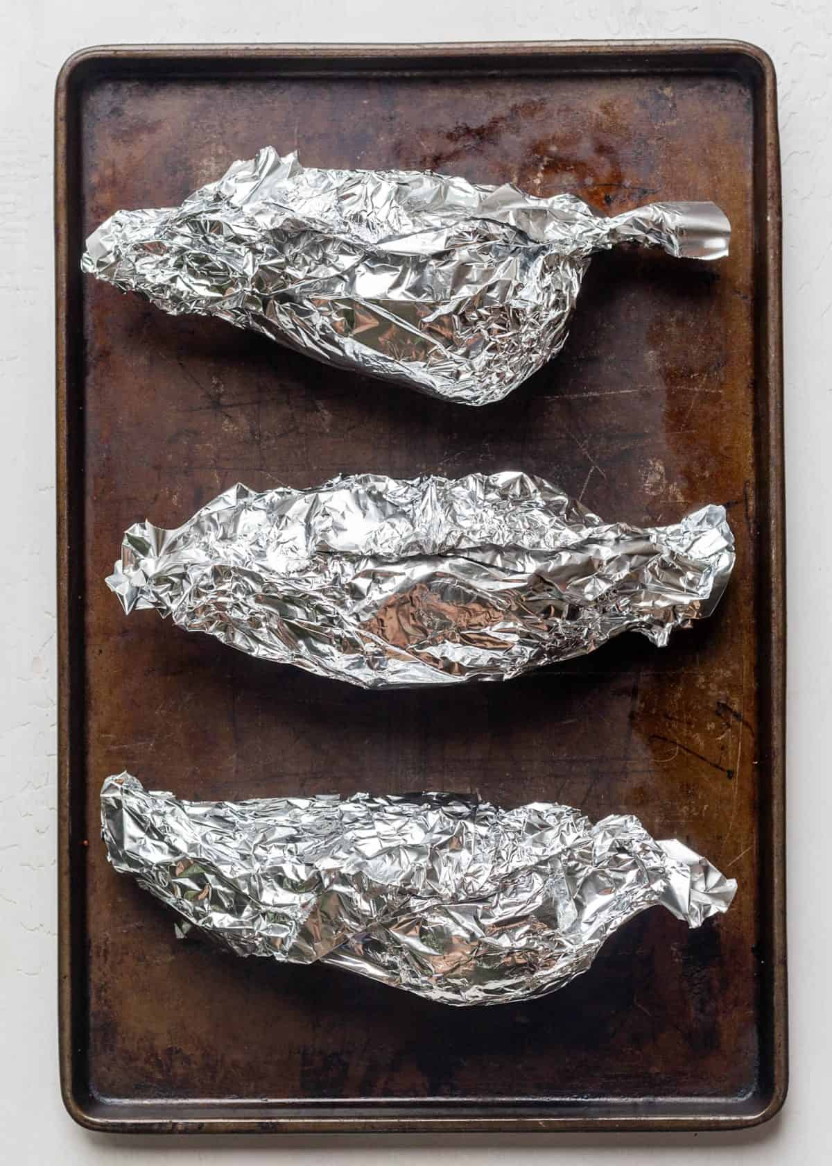making healthy sweet potato casserole recipe - 3 sweet potatoes wrapped in aluminum foil on a baking sheet.
