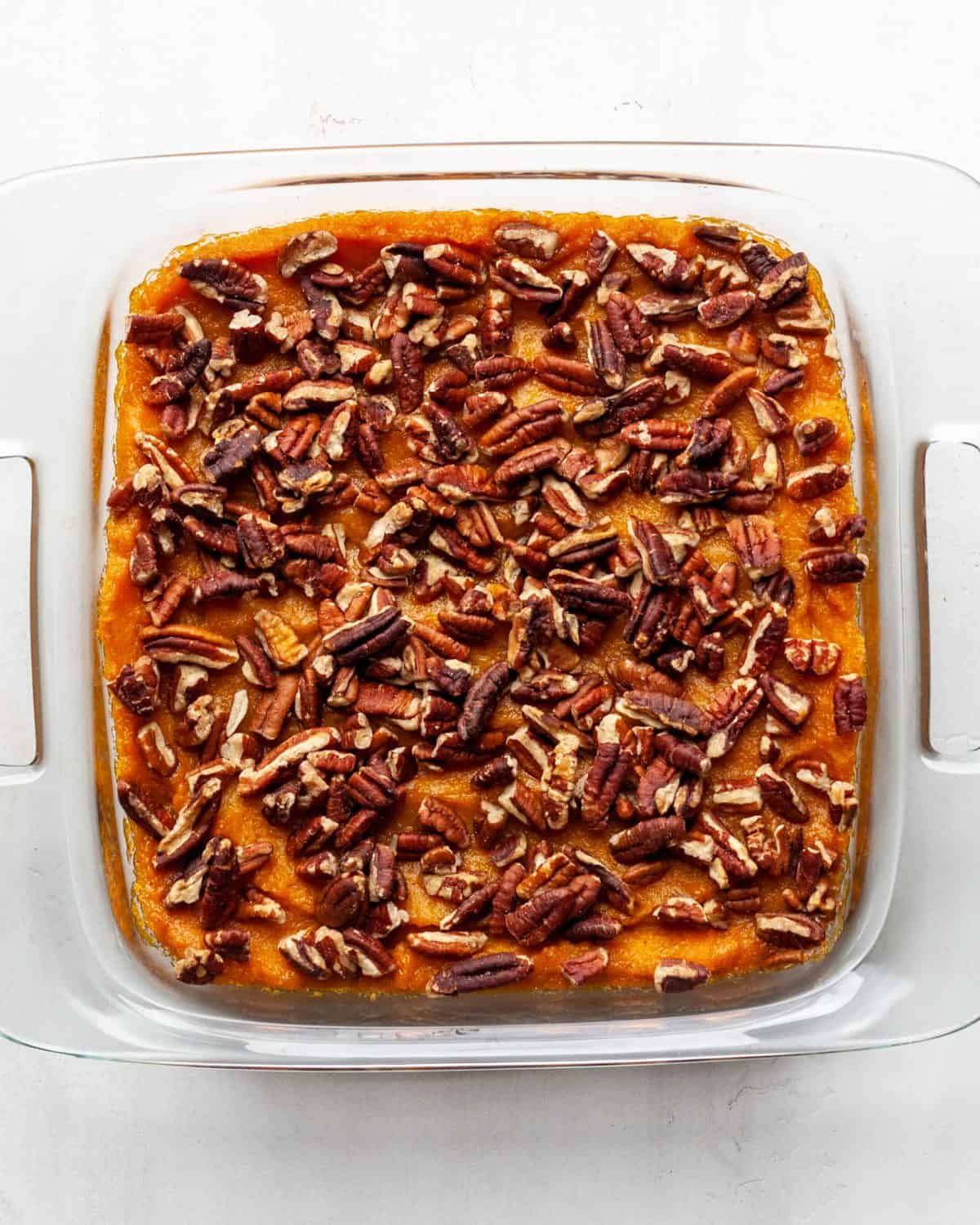 making healthy sweet potato casserole recipe - sweet potato casserole filling spread into a square glass baking dish topped with pecans