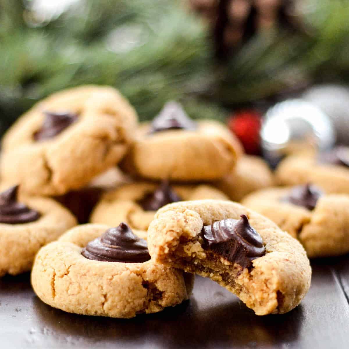 Front view of two Almond Butter Blossom Cookies stacked on each other, one with a bite taken out with a pile of cookies in the background