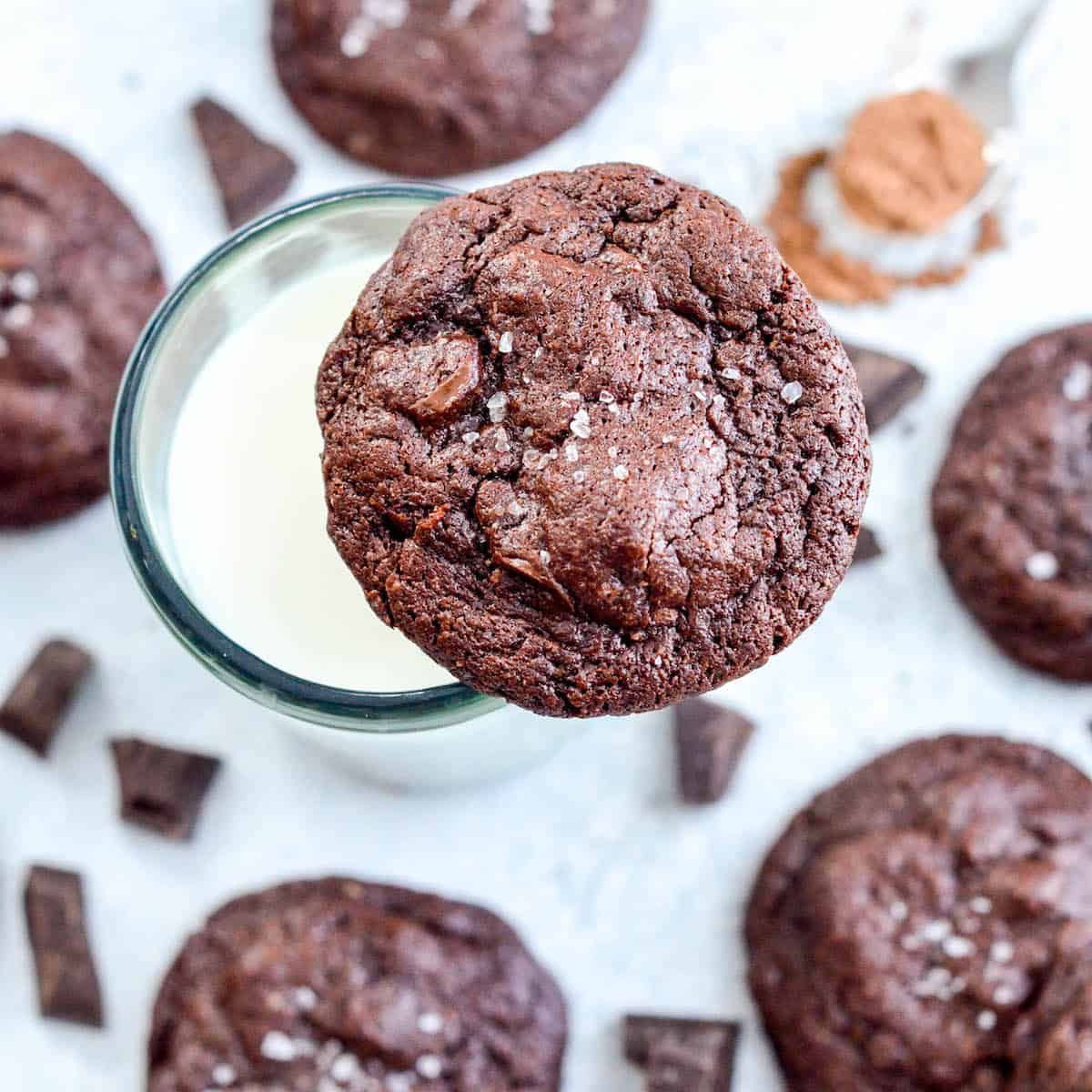 Overhead view of one Paleo Triple Chocolate Brownie Cookies resting on a glass of milk with seven other cookies surrounding it