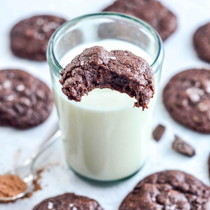 One Paleo Triple Chocolate Brownie Cookie with a bite taken out of it on a glass of milk with other cookies around the glass