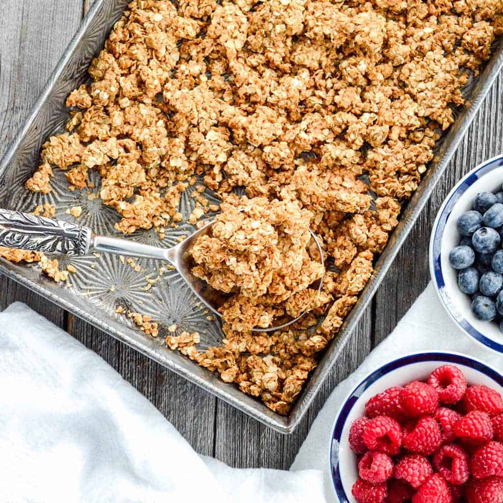 Overhead view of a pan of vegan healthy peanut butter granola with a spoon in it with a scoop of granola on the spoon. 