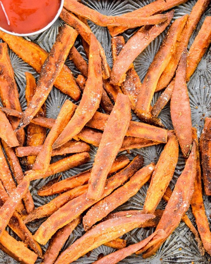Peanut Butter Crusted Sweet Potato Fries! An easy, healthy side dish recipe made with only 4 ingredients! A light crusting of peanut butter adds protein and makes these sweet potato fries irresistible! Gluten-free, dairy-free, sugar-free and vegan! #sweetpotato #fries #peanutbutter #vegan #glutenfree #dairyfree Overhead view of a baking sheet with Peanut Butter Sweet Potato Fries