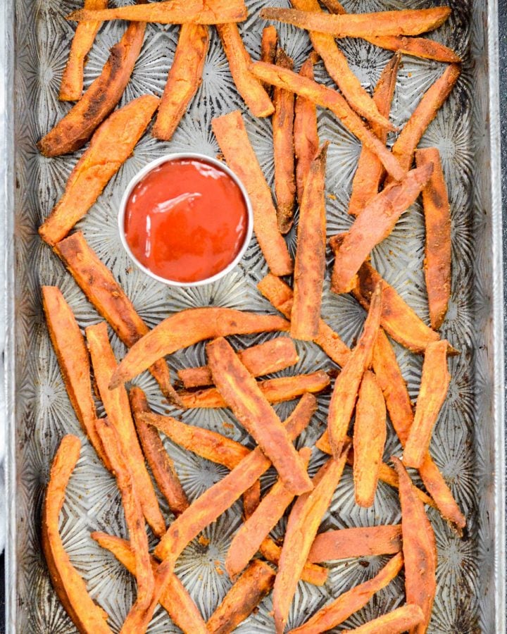 Peanut Butter Crusted Sweet Potato Fries! An easy, healthy side dish recipe made with only 4 ingredients! A light crusting of peanut butter adds protein and makes these sweet potato fries irresistible! Gluten-free, dairy-free, sugar-free and vegan! #sweetpotato #fries #peanutbutter #vegan #glutenfree #dairyfree Overhead view of a baking sheet with Peanut Butter Sweet Potato Fries