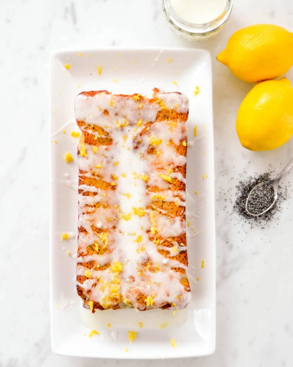 a loaf of paleo lemon poppy seed bread on a white platter with glaze before cutting. 