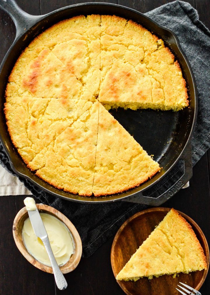 Overhead view of healthy skillet cornbread recipe in a cast iron skillet cut into 8 pieces with one removed on a plate next to the skillet